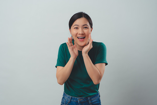 Asian woman happy smiling announcement making a telling secret gesture, sharing news, standing isolated on background.