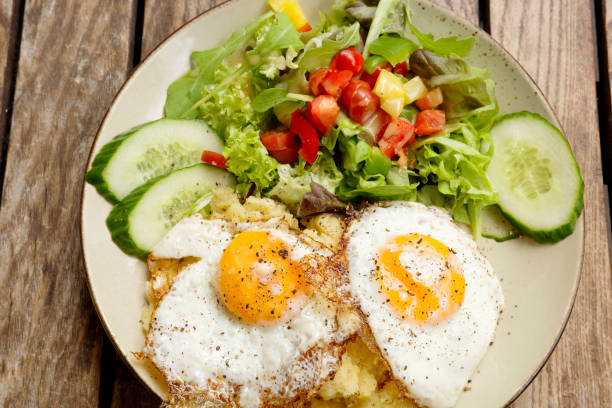 istock Fried eggs with fresh salad and potato mash outdoors on wood table 1486988331