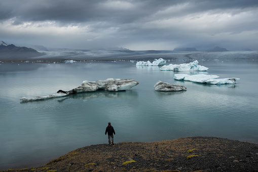 A lone male traveller, hiker, tourist observing the magnificent Vatnajokull glacier at the edge of atmospheric Glacier Lagoon in Iceland during day time.