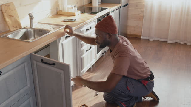 African American Plumber Working In Kitchen