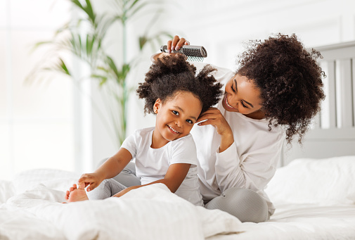 Happy ethnic family. African american mother brushing her little daughter's curly hair