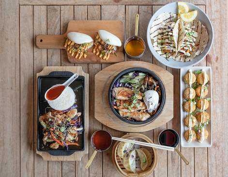 fusion food on wooden table , dumpling, steamed bao, bbq korean chicken