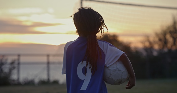 Sport, child and soccer player with football at sunset or night training, commitment and healthy exercise at school. Kid, athlete and outdoor field and love of game, fitness or sports education