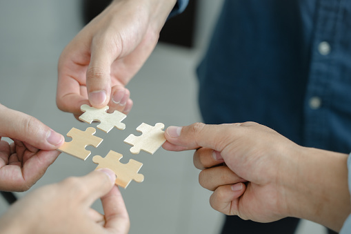 The concept of teamwork and partnership Hands joining puzzle pieces in office Businessmen put together a jigsaw puzzle - volunteer charity team business uniy.
