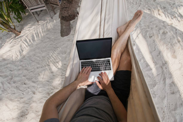workation, remote work, freelancer with laptop in hammock - on beach laptop working imagens e fotografias de stock