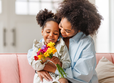Happy mother's day! Afro american family happy baby daughter congratulates mom on the holiday, hugs her and gives bouquet of flowers at home
