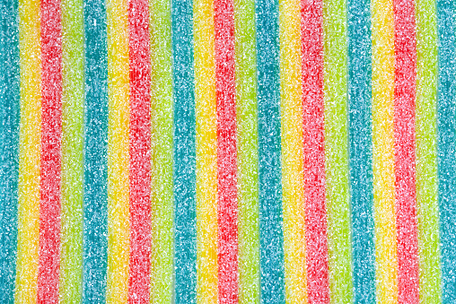 Colored jelly candy strips in sugar sprinkles, backdrop.
