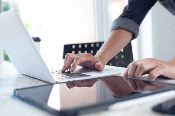 istock Closeup of business man hand typing on laptop computer and using digital tablet pc on table at home office. Designer working on design project, work from home, paperless office 1487007438