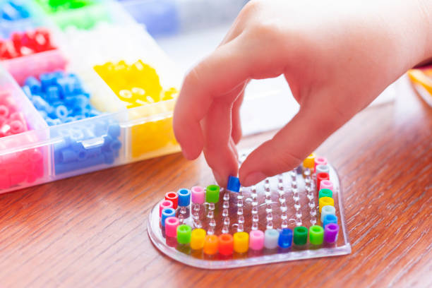 A child making a heart from plastic beads piece by piece. Educational activity for kids. Motor skills development. Creative craft