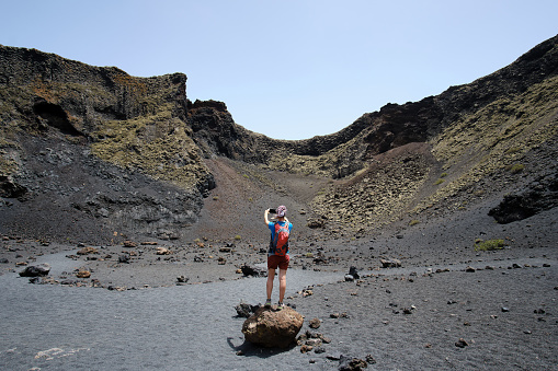 Woman with red backpack photographing from inside the crater of El cuervo volcano, Lanzarote. Canary Islands