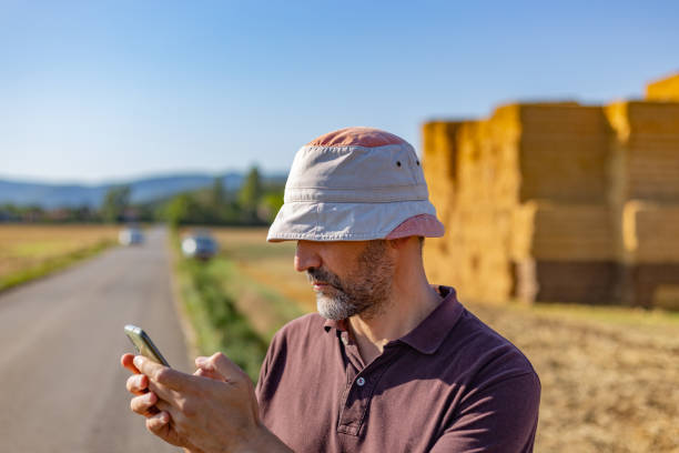 istock Half body view of man with hat using his mobile phone to request roadside assistance in rural environment. Bright summer morning 1487010317