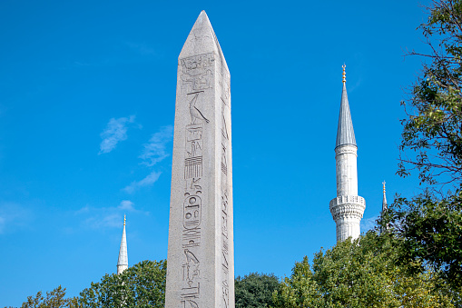 Istanbul Turkey: September 03 2022; Egyptian Obelisk of Thutmose III and minarets of Blue MosqueThe Hippodrome of Constantinople (Sultanahmet MeydanA) was a circus that was the sporting and social centre of Constantinople, capital of the Byzantine Empire and the largest city in Europe. Today it is a square named Sultanahmet MeydanA (Square) in the Turkish city of Istanbul, with only a few fragments of the original structure surviving. It is sometimes also called AtmeydanA (Horse Square) in Turkish.Emperor Theodosius brought an obelisk from Egypt and erected it inside the racing track. Carved from pink granite, it was originally erected at the Temple of Karnak in Luxor during the reign of Tuthmosis III in about 1490 BC. Theodosius had the obelisk cut into three pieces and brought to Constantinople. Only the top section survives, and it stands today where Theodosius placed it, on a marble pedestal. The obelisk has survived nearly 3,500 years in astonishingly good condition