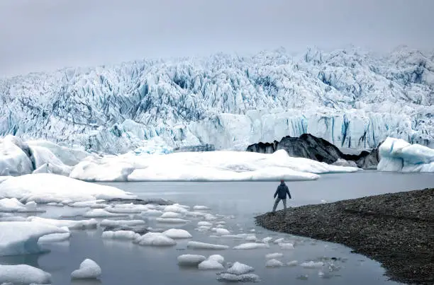 A lone male traveller, hiker, tourist at the edge of magnificent  Fjallsarlon Glacier Lagoon in Vatnajokull national aprk, surrounded by ice in scenic South Iceland