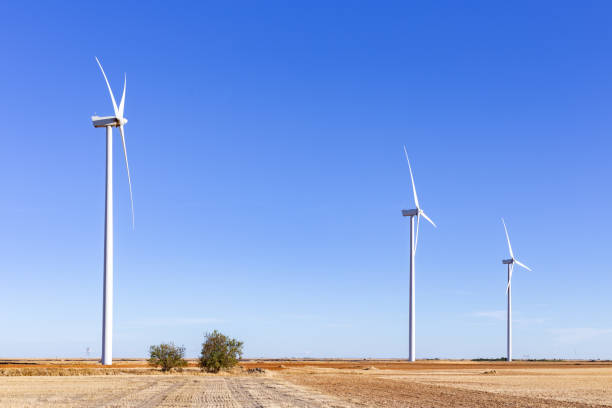 istock three wind power towers next to two trees. Clear sky 1487012230