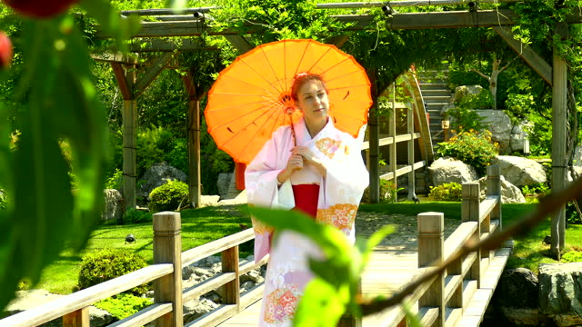 young woman in kimono walking in the park with sun umbrella