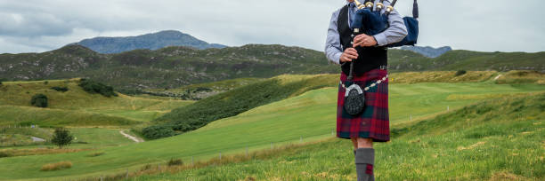 Scottish bagpiper in the Highlands of Scotland, panoramic mountains landscape background, UK stock photo