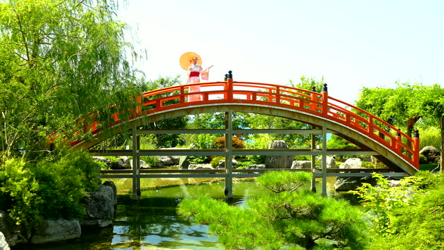 young woman in a kimono on a bridge over a pond in a Japanese garden