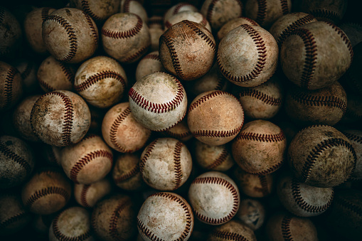The players' used baseballs are gathered and placed in a basket, with traces of the red dirt from the baseball field indicating that they have been used.