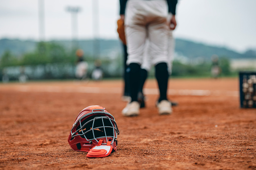 This is a stock photo or background image of a catcher's helmet lying on the baseball field, with players standing in the background.