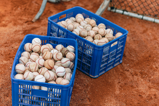 Baseball equipment including a basket full of baseballs and a protective net are located on the baseball field.