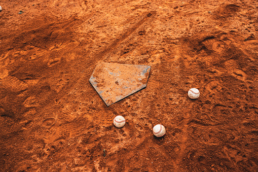 This is a photo of a home plate and scattered baseballs, presenting the post-game or practice condition of a baseball field.