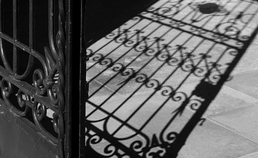 Silhouetted ancient open cast iron gate shadow, low angle view.  Antiquities. Lugo city cemetery doorway.