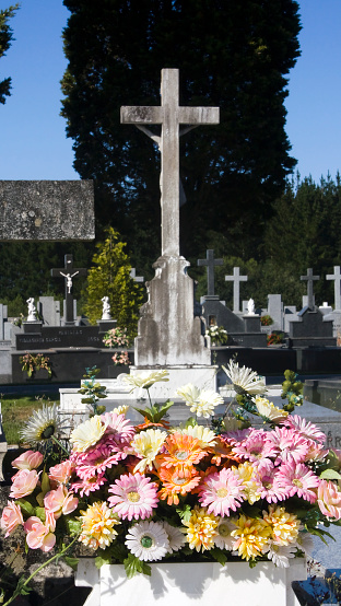 Ancient cemetery, group of  crosses  in the sunlight in Lugo city, Galicia, Spain. Multi colored flowers bouquet in the foreground.