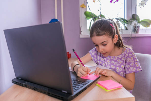 istock Adorable girl writes a notes while doing her homework with laptop computer at home 1487019272
