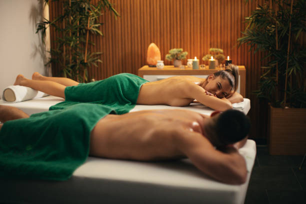Young woman and mid adult man relaxing in spa center and waiting massage together. Nice cozy space with candles in background make them feeling wonderful