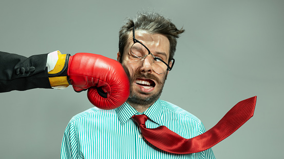Mature businessman in red tie getting boxing punch in jaw from business competitors. Concept personal challenge, financial loses, business fall, deadlines, economic crisis, bad investment. Sport, ad