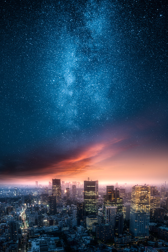 Dramatic view of a city skyline at night with red clouds painted by setting sun and beautiful milky way up on the sky