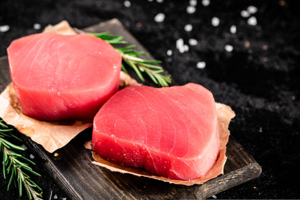 istock Raw tuna steaks on a rosemary cutting board. 1487028310