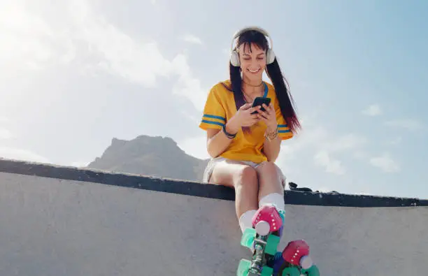 Photo of Relax, phone and music with woman and rollerblades for skating, streaming and social media app. Technology, headphones and sports with girl in skate park for internet, mobile radio and fitness