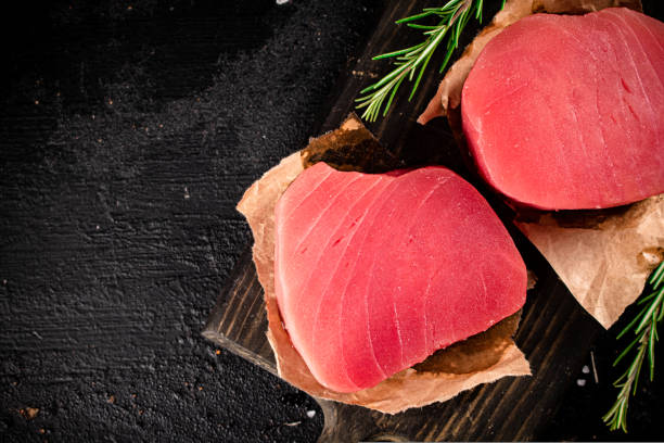 istock Raw tuna steaks on a rosemary cutting board. 1487028386