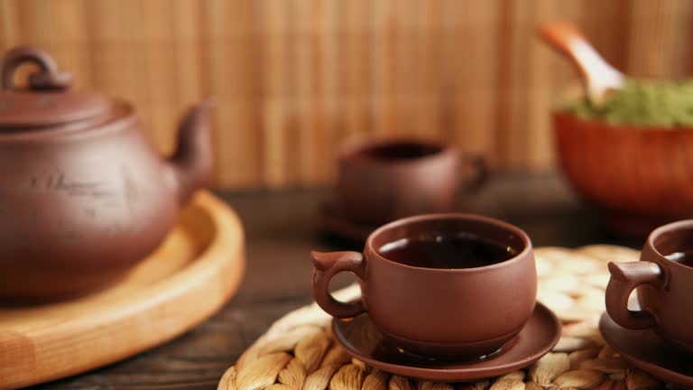 Tea Ceremony. Traditional Asian Tea Utensil, Serving Authentic Set. Person Pouring Tea from Brown Pottery Teapot to Teacup. Bamboo Tray. Lifestyle. Wellness Balance Health. Tea Brewing Equipment