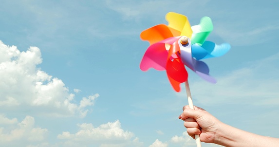 Motion blurred of colorful pinwheel. Woman hand holding colorful plastic windmills on blue sky background. Green energy concept