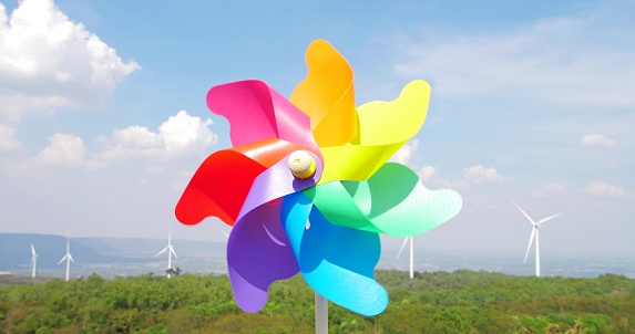 Close up colorful windmill toy on natural mountain with high wind turbine park and blue sky background