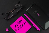 Blogging, recording or listening to podcasts, remote working, freelance concept. Mobile phone, glasses, pen and a piece of paper with the words Audio podcast to indicate e-commerce or part-time work.