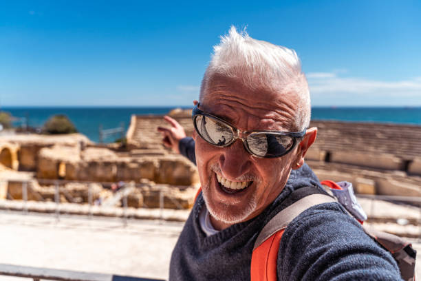 handsome middle aged man visiting tarraco archaeological complex, Tarragona - Happy tourist taking a selfie in front of roman ruins stock photo
