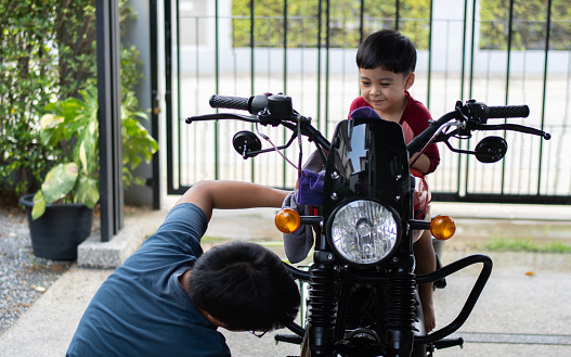 Middle age Asian father with his toddler son washing motorcycle together outdoors. Family toget her activity