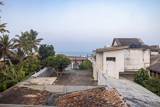 Galle, Sri Lanka - February 13th 2023:  View over roof tops to coconut palms and a calm Indian Ocean