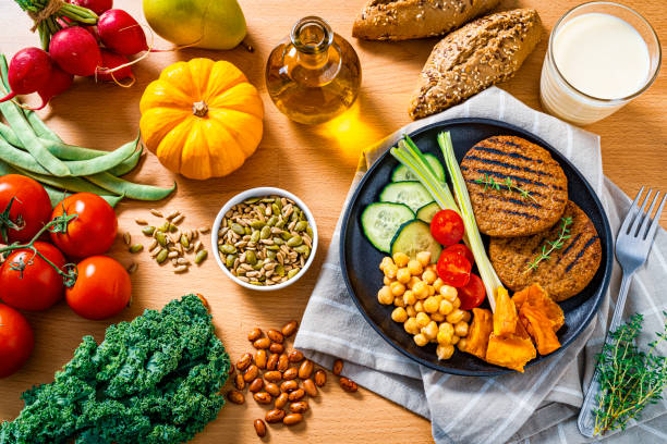 Overhead view of wooden table filled with a colorful healthy plant-based food. A plate with plant-based patties and fresh vegetables is at the right. High resolution 42Mp studio digital capture taken with SONY A7rII and Zeiss Batis 40mm F2.0 CF lens