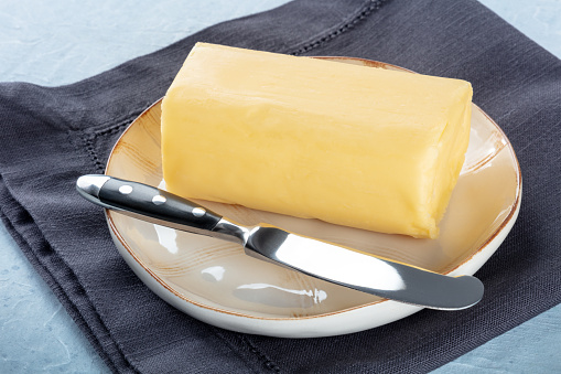 A stick of fresh butter with a knife on a plate, on a slate background, cooking ingredient