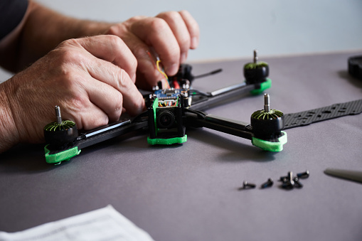 Close up of man's hands assembling a drone from parts, using tools, Preparing high speed racing quadcopter for flight. Repair drone before training process.