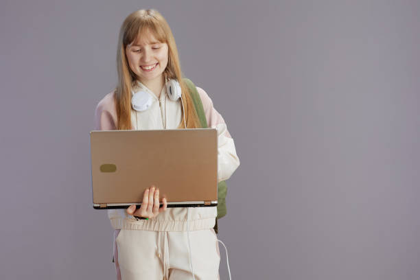 istock smiling modern girl in beige tracksuit using laptop 1487041928