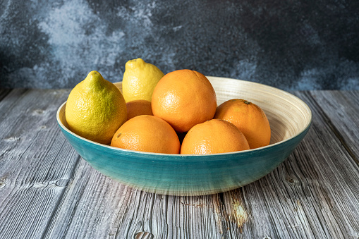 Blue bamboo wooden fruit bowl with Valencian oranges and lemons on wooden table