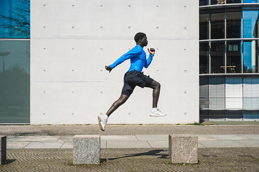 young sportsman jumping on stone blocks in front of concrete wall outdoors in berlin at sunny day