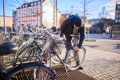 Senior man locking the back wheel of his bicycle at a sidewalk bike rack in the city