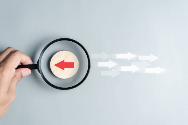 istock Hand holding magnifier focus to Red arrow and different direction facing opposite direction with white arrow for business disruption and technology transformation and different thinking idea concept. 1487050707