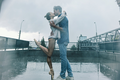 a partner in love kisses a ballerina in the rain while walking around the city